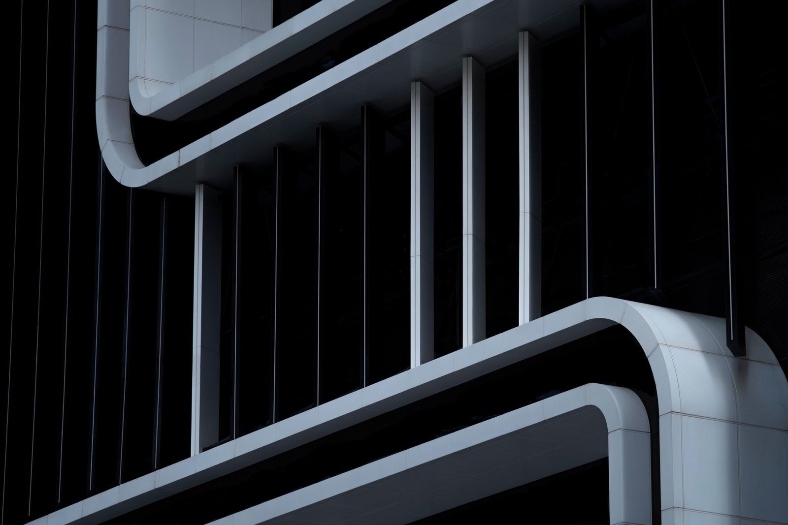 Dark building facade where rounded white floor bands stack one above another, linked by slim vertical fins against black glass