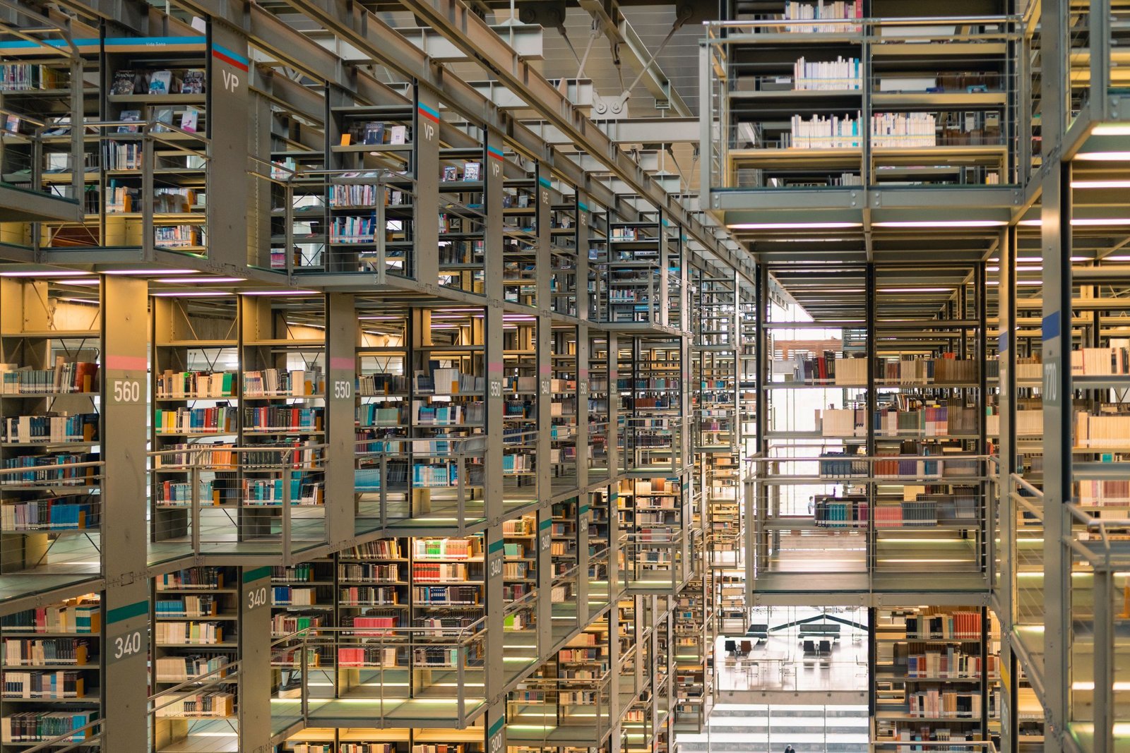 Suspended steel bookstacks rising through a vast library atrium, numbered shelves of books receding in layers towards daylight